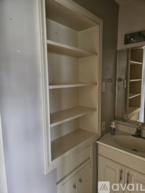 A white cabinet with shelves and a sink in front of a mirror.