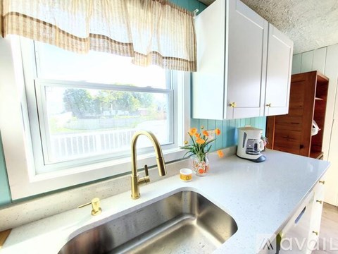 A kitchen with a window overlooking a fence and a sink with a gold faucet.