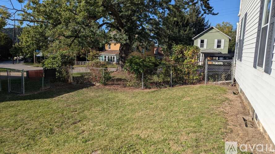 A backyard with a fence, a tree, and a house in the background.