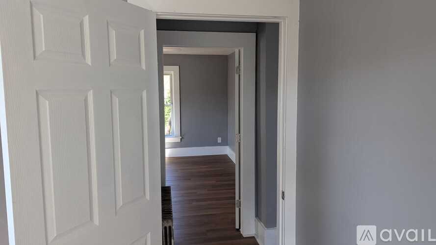A white door is open to a hallway with wood flooring.