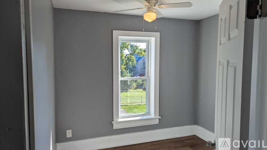 A room with a ceiling fan and a window showing a view of a lawn and trees.
