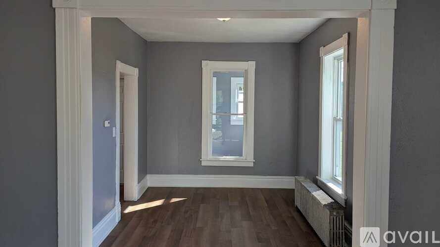 A room with grey walls and wooden flooring, featuring a window and a radiator.