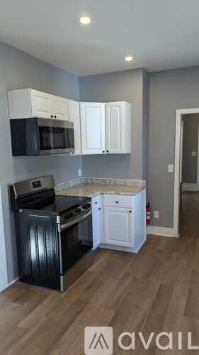 A kitchen with a black oven and microwave, white cabinets, and a wooden floor.