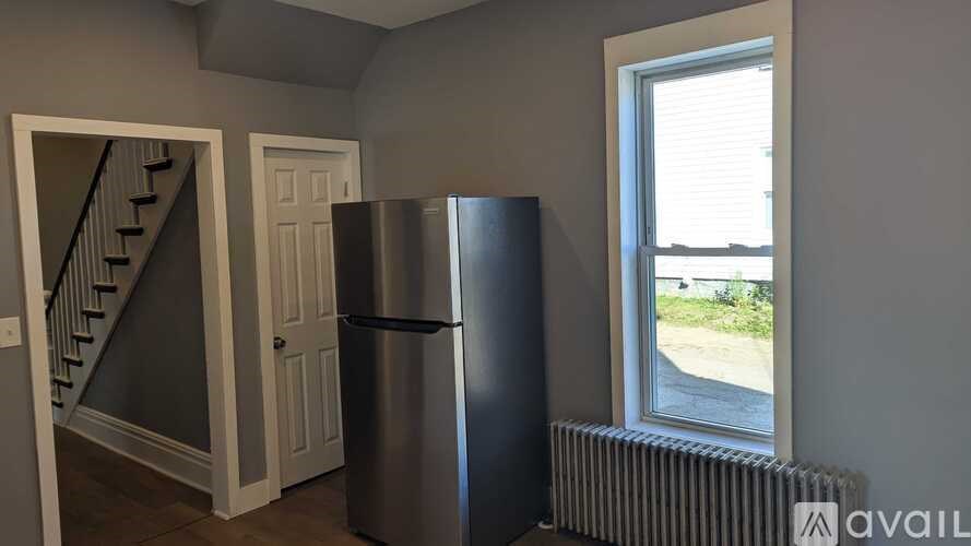 A room with a staircase, a door, a window, and a fridge.