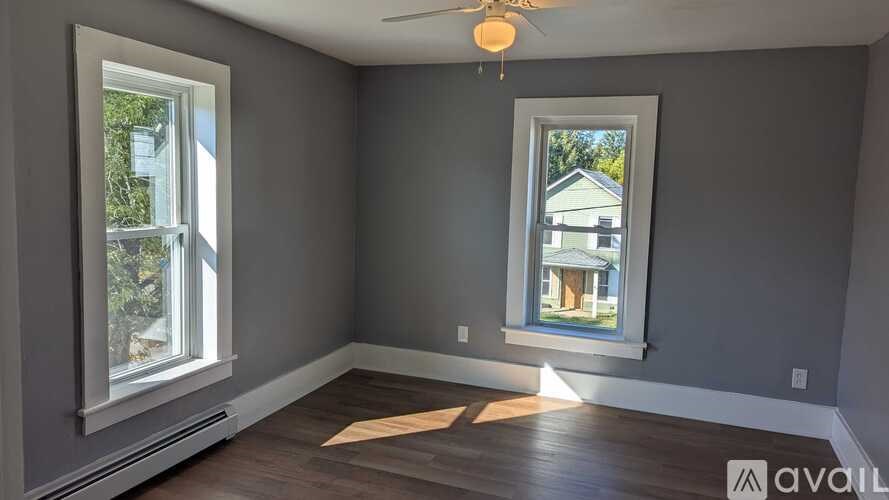 A room with a ceiling fan and two windows.