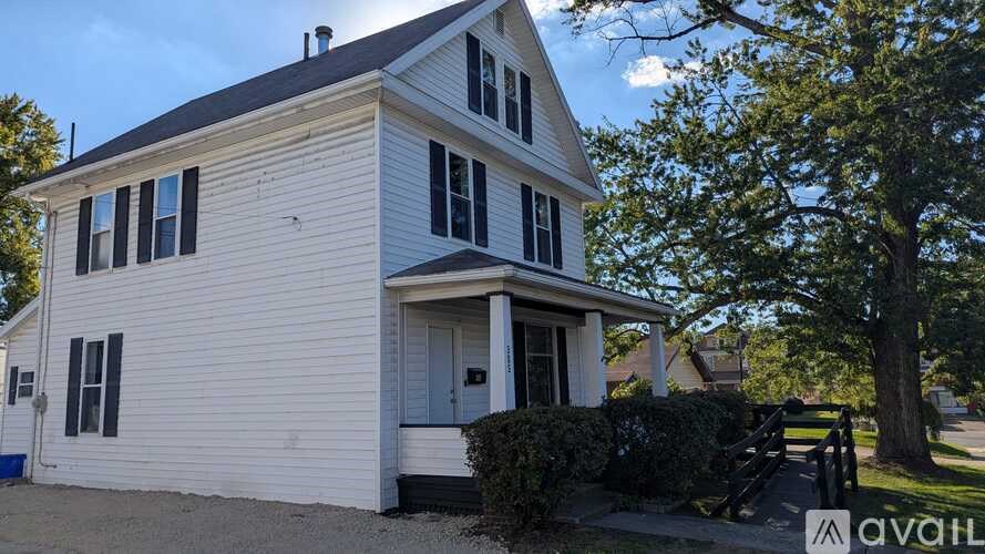 A white house with a grey roof and a tree in front.