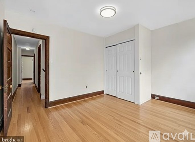 A room with wooden floors and white walls, with a door and a mirror on the left side.
