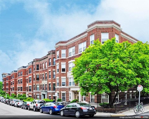 A street view of a row of parked cars in front of a red brick building.