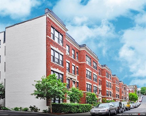 A row of red brick apartment buildings with green trees in front.