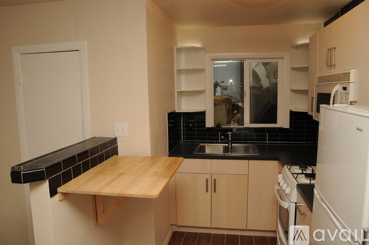 A kitchen with a white fridge, black countertops, and a wooden table.