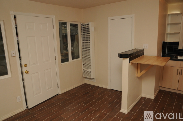 A kitchen area with a white door, a window with blinds, and a wooden countertop.