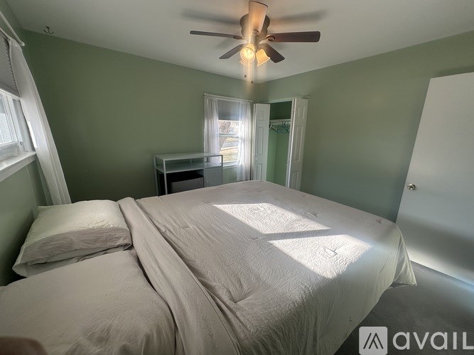 A bedroom with a bed, a ceiling fan, and a window with sunlight coming through.