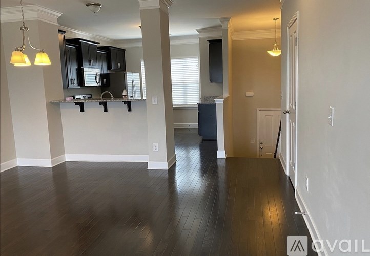 A spacious living room with hardwood floors and a kitchen area in the background.