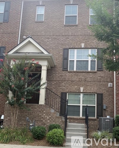 A brick building with a black railing and a tree in front.