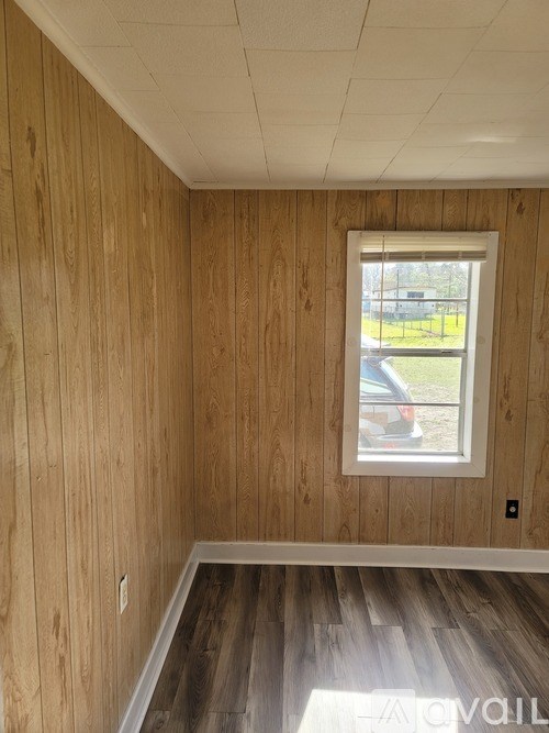 A room with wooden walls and a window showing a parking lot outside.