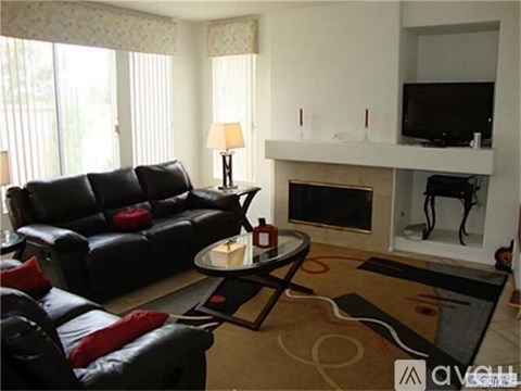 A black leather couch with red pillows sits in a living room with a fireplace and television.