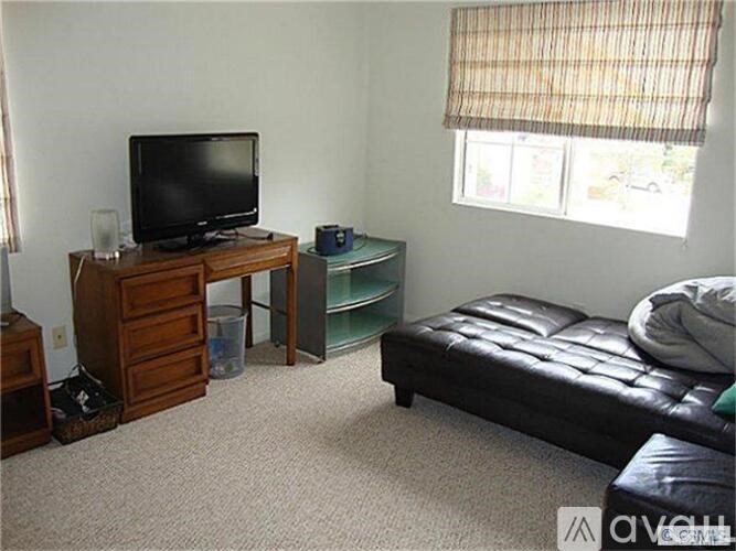 A living room with a black leather couch, a television, and a window with blinds.