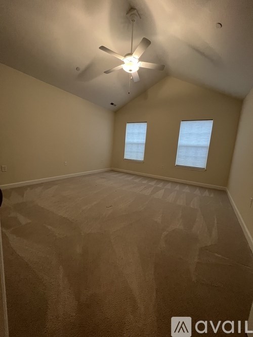 A room with a ceiling fan and two windows.