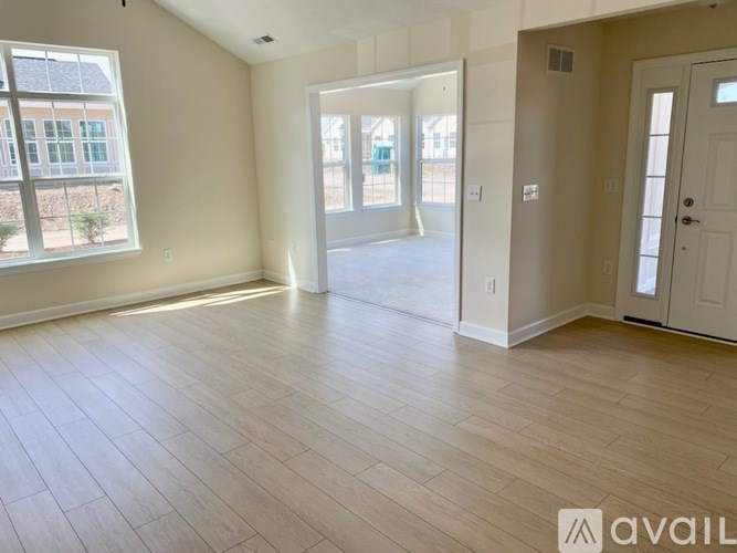 A spacious room with light wood flooring and white walls.