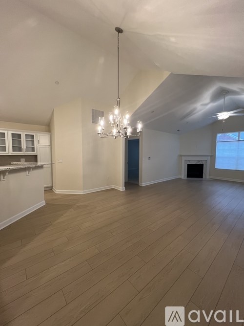 A spacious room with wooden flooring and a chandelier hanging from the ceiling.