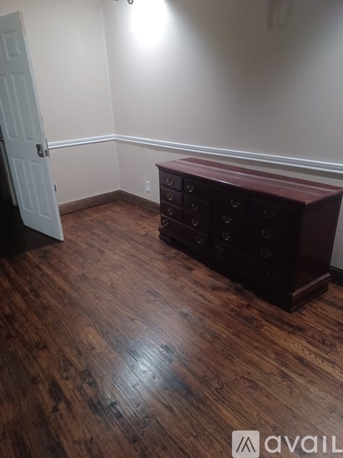 A room with a wooden floor and a brown chest of drawers.