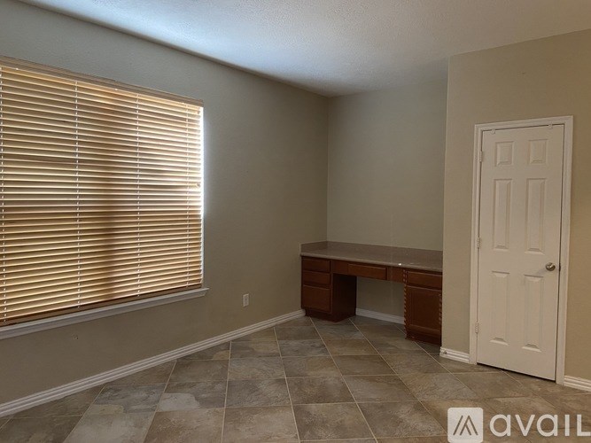 A room with a desk and a window with blinds.