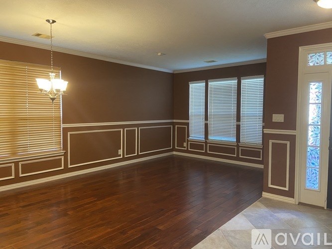 A room with brown walls and wooden flooring, featuring a chandelier and a door.
