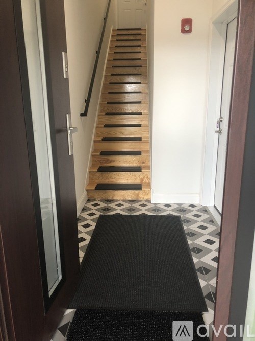 A hallway with a black mat in the foreground and a staircase with wooden steps.