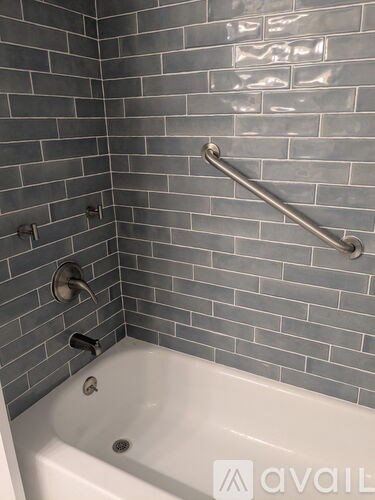 A bathroom with a white tub and grey tiles.