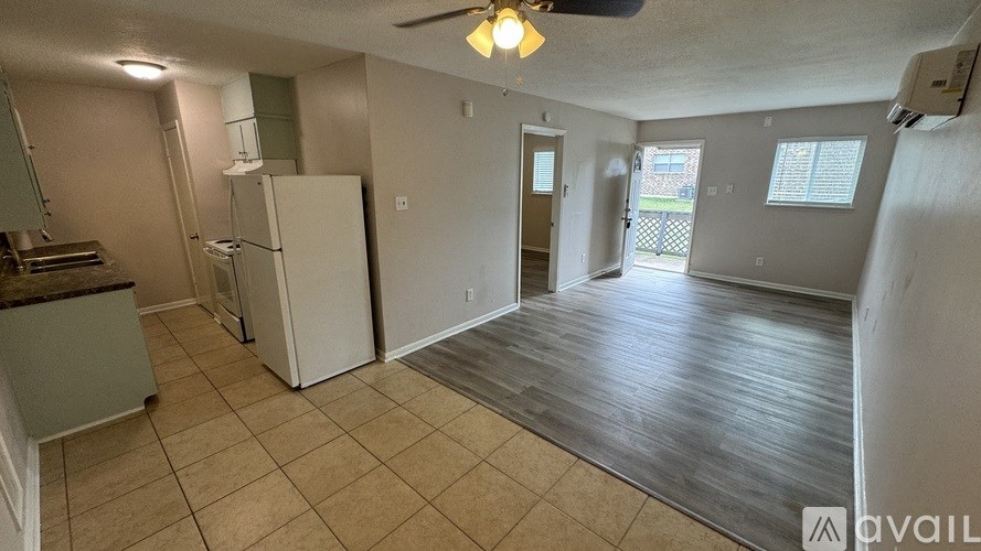 A spacious living room with a kitchen area and a ceiling fan.