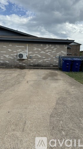 A grey building with a blue bin in front.