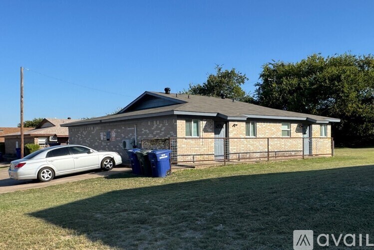 A house with a car parked in front and a blue trash bin to the side.