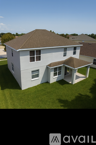 A house with a brown roof and white walls is surrounded by a grassy lawn.
