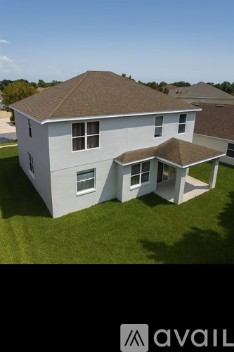 A house with a brown roof and white walls is surrounded by a grassy lawn.