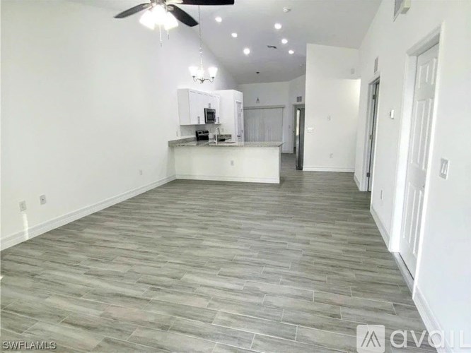 A spacious room with a ceiling fan and a kitchenette in the background.