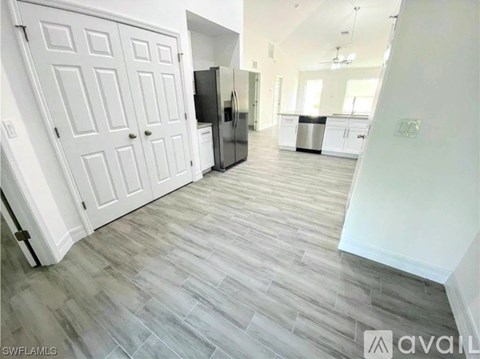 A kitchen with white cabinets and a refrigerator is visible from the hallway.