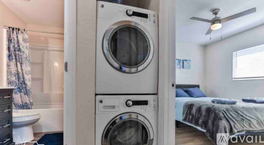 A washer and dryer stacked on top of each other in a small room with a bed and a window.