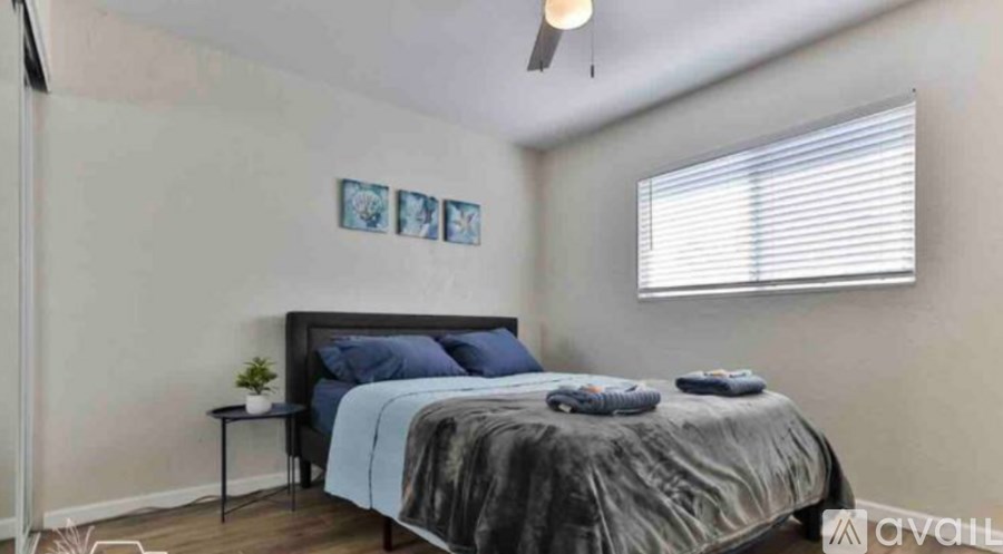 A bedroom with a bed, a small table, and a window with blinds.