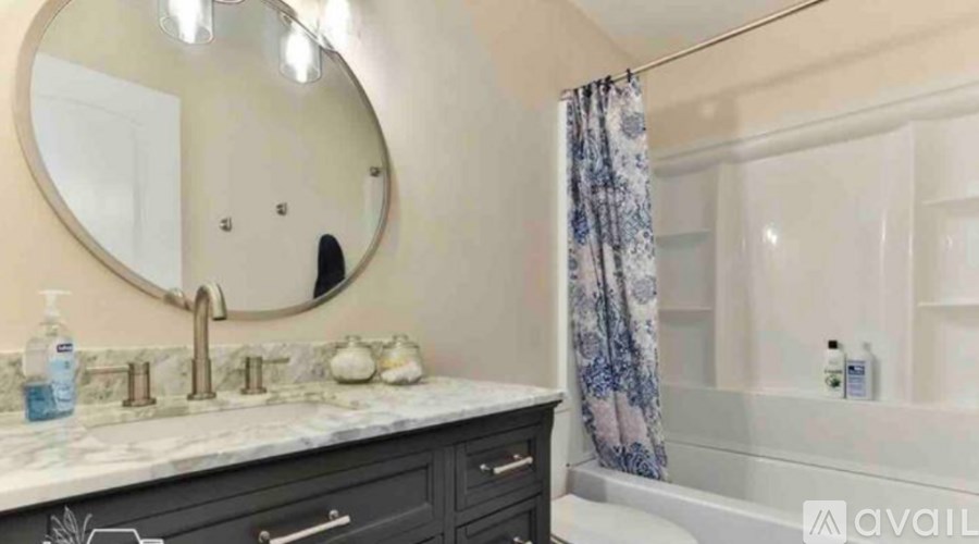 A bathroom with a marble countertop and a round mirror above it.