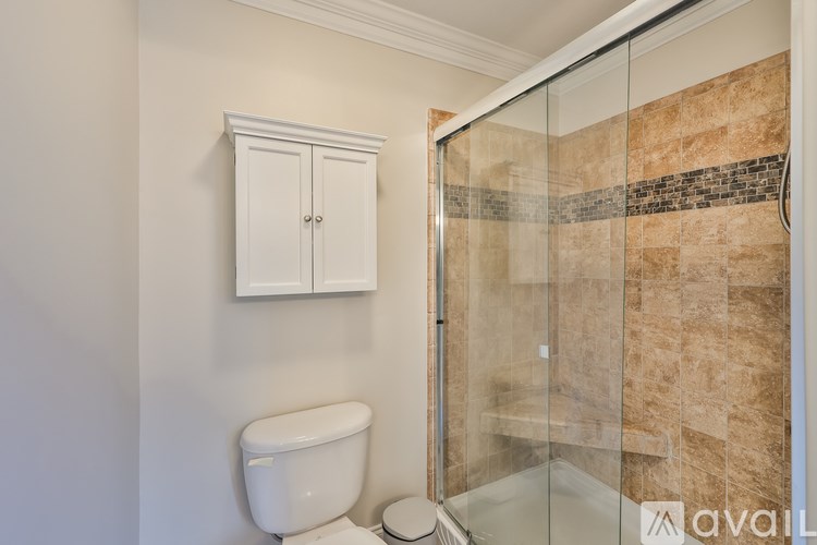 A bathroom with a toilet, a cabinet and a glass shower door.