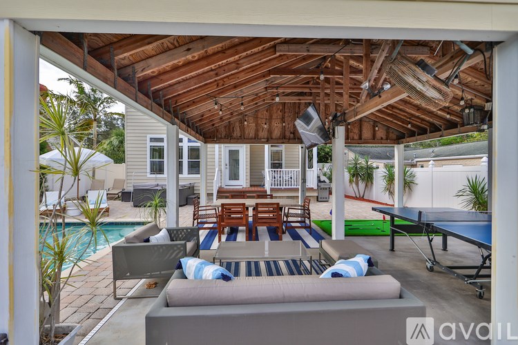A patio with a table and chairs is covered by a wooden roof.
