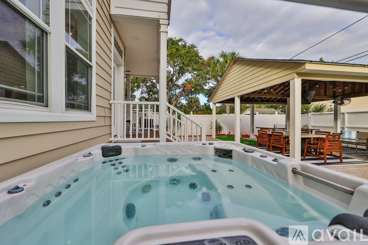 A hot tub is in the middle of a patio with a white railing and a covered table.