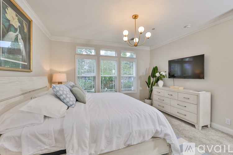 A bedroom with a large bed, a chandelier, and a television on the wall.