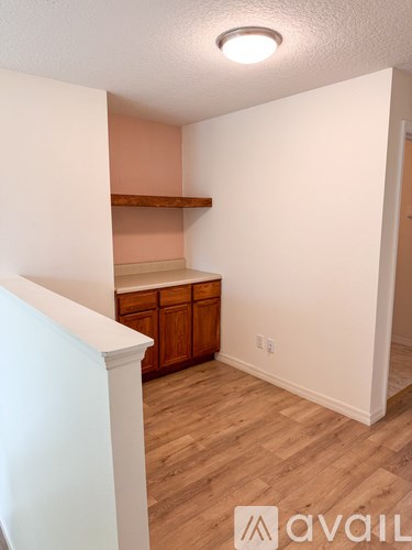 A room with a wooden floor and a white wall with a shelf and a cabinet.