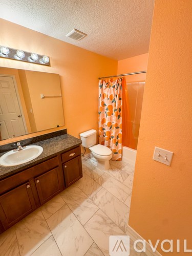 A bathroom with orange walls, a sink, toilet, and a shower with a curtain.