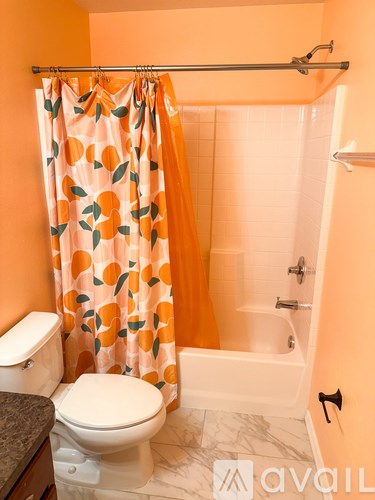 A bathroom with orange walls and a shower curtain with orange and green leaves on it.