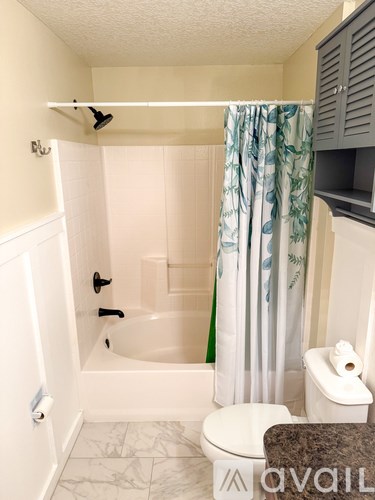 A bathroom with a white tub and toilet, a shower curtain, and a cabinet.
