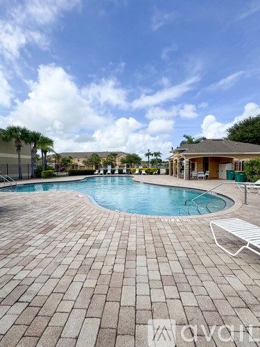 A pool surrounded by a brick patio with a white chair.