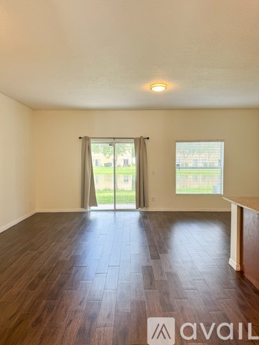 A room with wooden flooring and a window with a view of a green area outside.