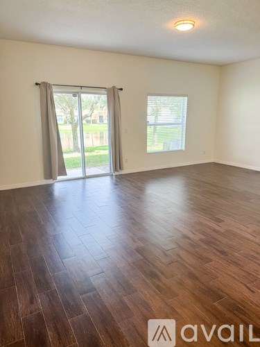 A room with wooden flooring and a window with a view of a green area outside.